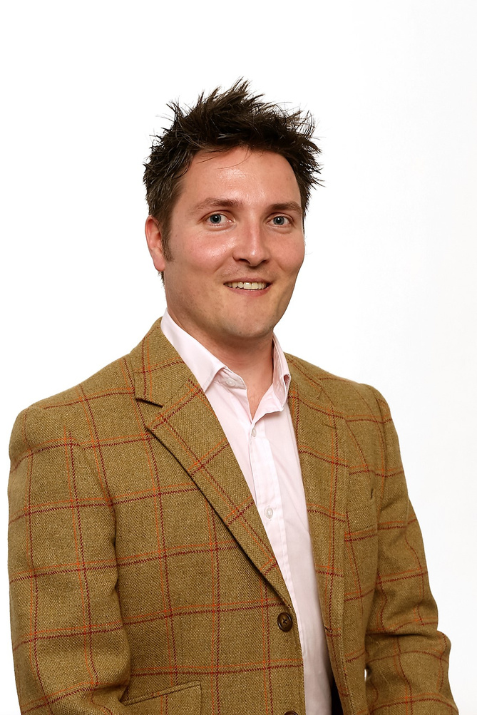a portrait of Jamie Carrahar wearing a pink shirt and tweed jacket